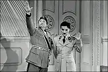 Two actors costumed in military uniforms portray fictional dictators performing salutes