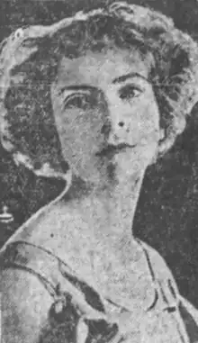 A grainy black-and-white photograph of a young white woman with short curly bobbed hair; she is wearing a dress with a scooped neck and bare shoulders