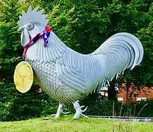 The sculpture, facing left, wearing a gold medal labeled "London 2012" with a red and blue knitted ribbon