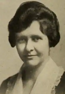 A young white woman with dark hair in an updo, wearing a blouse with a wide white collar edged in ruffles