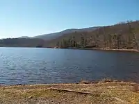 View of the Douthat State Park lake from boat launch area showing blue sky, trees, mountains and water