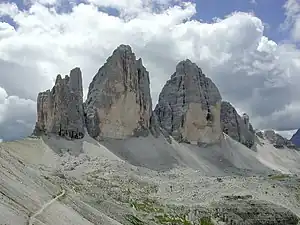 Three distinctive rock faces jut out above a sandy mountainside