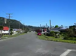 Centre road stretching into distance with grass verges and buildings at both sides and a bright blue sky