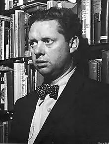 A black and white photograph of Thomas wearing a suit with a white spotted bow tie in a book shop in New York.