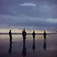 An album cover showing four men in silhouette standing on a wet beach. There are dark clouds in the sky and the sun is low on the horizon. The album's name and the band's name is in white letters in the top centre of the album cover.