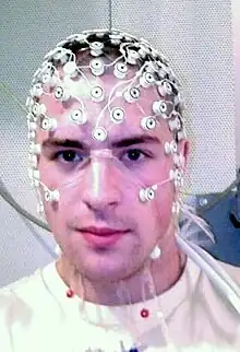 Photo of man wearing multiple electrodes on his head, with wires connecting to a computer