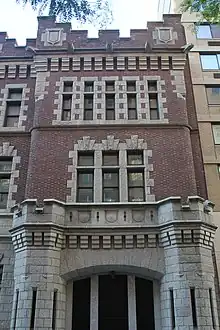 The First Battery Armory's western pavilion as seen from across 66th Street. The ground story contains a granite arch with a garage door, while the second and third stories contain a brick facade with granite-trimmed windows.