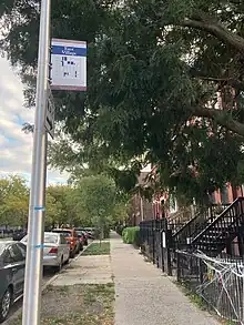 A street sign on a sidewalk. On the top, it reads: "East Village." In the middle is a map highlighting the area of the East Village. On the bottom, it reads: "This ensemble of worker's cottages and two- and three-flats was originally home to German, Polish, and other European immigrants who settled in the area in the 19th century. The District forms one of Chicago's earliest-surviving working-class neighborhoods.