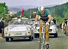 A man on a bicycle, with a car behind him.