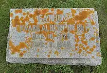 Grey granite stone partially covered in orange-coloured lichen, inscribed with Gilroy's name, birth and death years