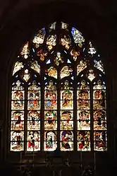 The chevet window with scenes from the Passion (Christianity). Scenes in the top row depict the raising of Lazarus, the entry into Jerusalem,  the last supper and Joan of Arc on horseback. In the next row is a scene depicting Jesus in the garden of olives, then his arrest and his being ridiculed, his appearance before Herod, the flagellation with Jesus tied to a tree, the carrying of the cross. In the lower row are two scenes involving the crucifixion, then Jesus being brought down from the cross and the preparation for his burial (the "Mise au Tombeau" followed by Jesus resurrected and emerging from the tomb and then his descent into limbo to save some souls trapped there