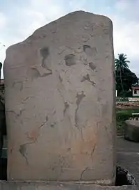 An upright stone slab with faint relief sculpture, badly flaked in places.