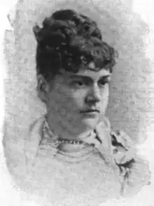 Portrait of a white woman with dark curly hair in an updo. She is wearing a light-colored garment, with beads at her throat.