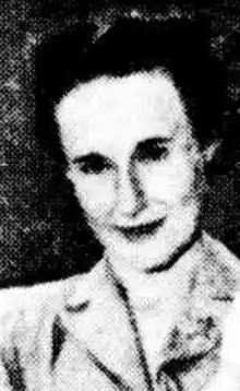 A white woman with dark set hair, wearing a notch collared blouse.