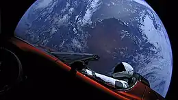 A mannequin (Starman) in a spacesuit drives a car with the Earth in the background