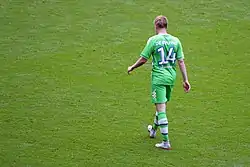 A colour photograph of Kevin de Bruyne, face back to the camera, wearing an all-green kit.