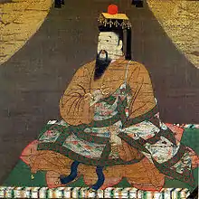 Emperor Go-Daigo wearing a benkan (Bunkan [ja] Buddhābhiṣeka, "Silken Painting of Emperor Go-Daigo"). A benkan board with gold leaf is placed on top of the hanging tail crown, and a sun decoration is placed on top of it. A bridle hangs from the crown board.