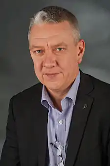 Head and torso of a man in his late 30s or early 40s, with brown hair and wearing a blue shirt.