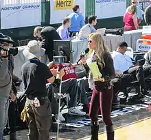 Erin Andrews is seen from a distance holding a microphone as she speaks to a camera