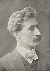 black and white right-face portrait of a man with bushy hair and moustache in formal attire