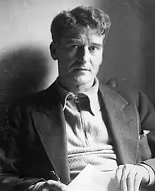 "Black and white photograph of O'Malley, showing his head and bust, a clean-shaven man with abundant wavy hair in his late thirties wearing jacket but no tie"