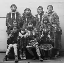 A group of eleven Alaska Native people, photographed in 1894. They are wearing fur jackets and leggings. Four of them are children.