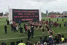 A team of female footballers run towards a banner