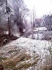 Late snow covers a meadow and brook bank.