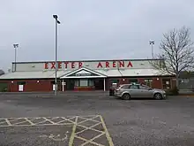 Image of the front of the arena stand, showing the car park and front doors