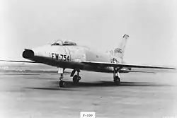 A jet aircraft with nose air intake sits on the tarmac, wearing U.S. Air Force insignia and "FW-754" coding on the nose