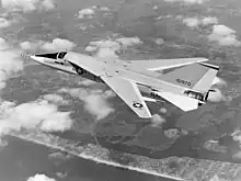 Black-and-white photo of jet aircraft flying above scattered clouds with wings swept back.