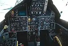 Cockpit of jet fighter with circular dials and gauges: A control stick protrude from between where the pilot's legs would be.