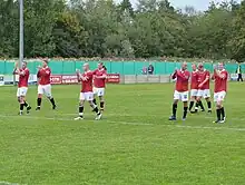 Eight F.C. United players at the edge of the penalty box after a game. Six of the players are clapping the fans.