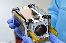 A scientist holding a PicoSatellite with gloves on after creating it.