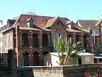 Multi-story brick house with peaked tile roof and decorative arches along the length of the second-floor balcony