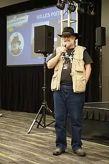 Poitras standing next to a stage holding a microphone.