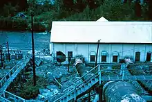 A low building by a river with hydraulic pipes feeding into it and a hole in the wall