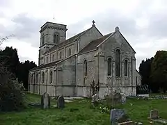 Gray stone building with square tower at far end. Grass and gravestones in the foreground.