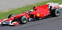 A red single-seater racing car is driven around a tarmac course.