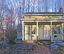 Photograph of a yellow house with white porch pillars and a center door with a window on either side