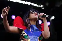 M.I.A. wearing sunglasses dressed in a blue-and-red outfit