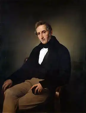 Painted portrait of a man seated in a chair, wearing a 19th-century suit, with a black jacket, white shirt, and brown trousers. He has short brown hair and is sitting in front of a brown background.