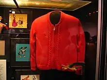 An orange sweater in a museum display. It has a zipper down the middle and a decorative cable pattern on either side of the zipper