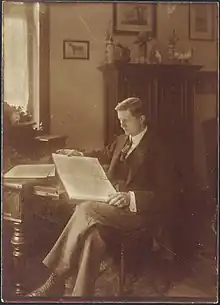 young white man, clean shaven, with full head of dark hair, neatly cut, sitting at a desk and looking at a musical score