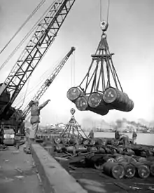 Several barrels being lifted off a ship by a crane