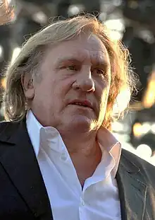 A man with long hair in an open-necked white shirt and grey jacket