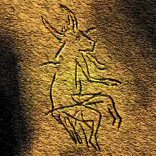 A black-and-white painting on a cave wall of a creature with horns, an animalistic face, and human limbs with a bipedal stance