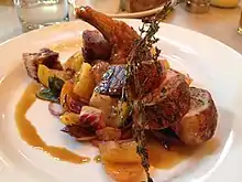 A sliced, cooked game hen with herbs on a plate.