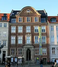 Five storied attached brick dwelling on the street. Elaborate ornamentation such as a large gable with curved roof, cornices and stone work around the rounded arch entrance.