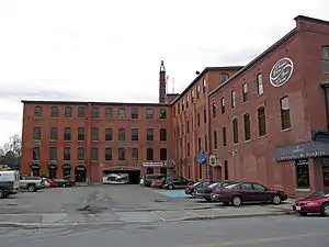 Four-storey red-brick factory building, with a parking lot and candy store in the foreground